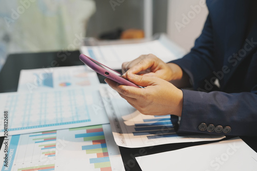 Fotografie A corporate worker holding up a financial report spreadsheet over a desk clutter