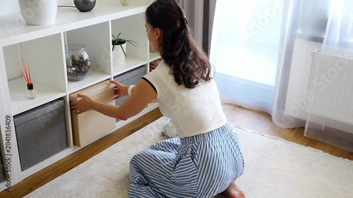 Young woman using storage box from shelving system in home interior. Home organization and decluttering routine concept