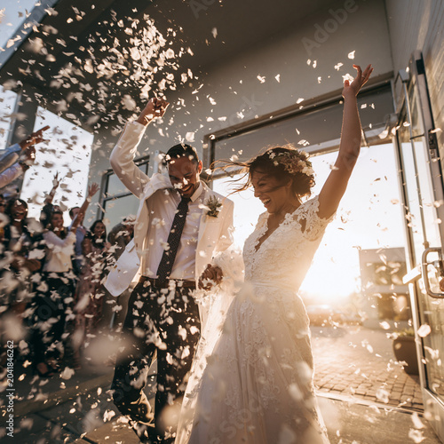 Couple celebrates wedding day with guests as they walk through flower petals at sunset in a modern venue