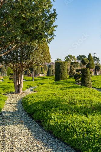 Landscaped park featuring intricate topiary designs. Various geometric shapes—cones, spheres, and rectangles—are created from densely packed shrubbery. Park 