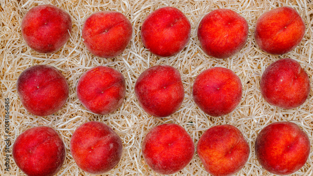 Fototapeta premium Fresh peaches arranged on a bed of straw in a market setting during midday
