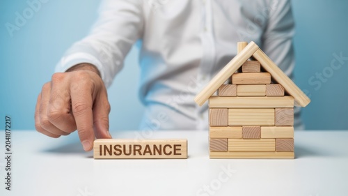 Hand Placing Insurance Block Near Wooden House Model Home Insurance and Property Protection Concept