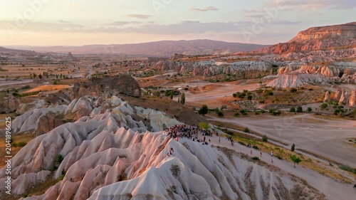 Aerial view of Rose Valley, Cappadocia, Turkey at sunset. Tourists gather with ATVs for quad biking among fairy chimneys and soft pink rock valleys.