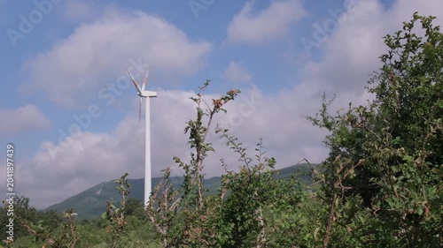 Wind turbine standing in a green rural landscape under a blue cloudy sky, symbolizing renewable energy