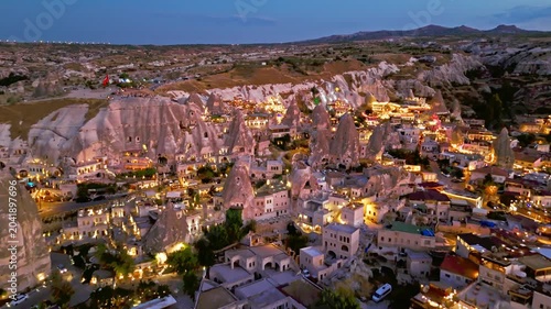 Aerial view of Goreme, Cappadocia, Turkey. Fairy chimneys and cave rocks rise above warm village lights at twilight.