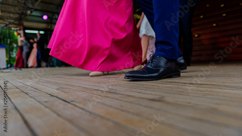 Fragment of a womans pink dress and mens shoes on a wooden floor during a dance.
