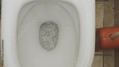 Top down view of a dirty white toilet flushing. Bubbling water swirls and drains away in the ceramic bowl during a daily hygiene routine