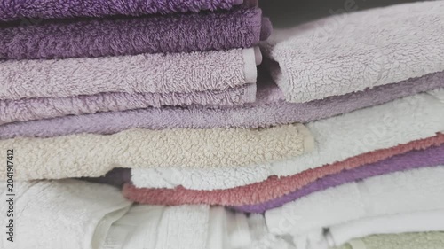 Detailed close up of neatly arranged terrycloth bath towels in an assortment of colors, such as purple, white, and pink, neatly piled on a shelf