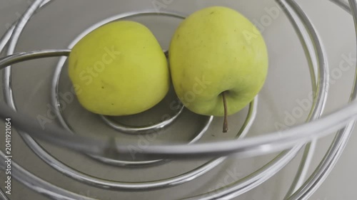 Pair of ripe yellow apples sitting inside a stylish, spiral metal fruit bowl. Modern kitchen interior and healthy food concept