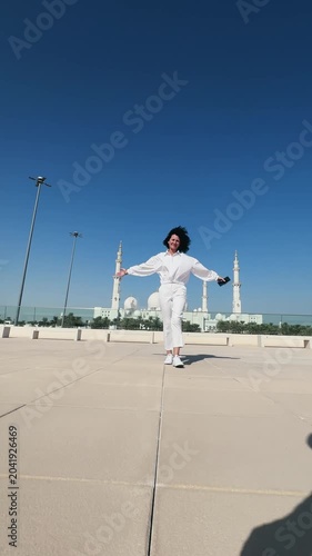 Cheerful tourist stylish woman dressed in white walk with outstretched arms near Sheikh Zayed Mosque in Abu Dhabi, United Arab Emirates, concept of victory and success, vertical video