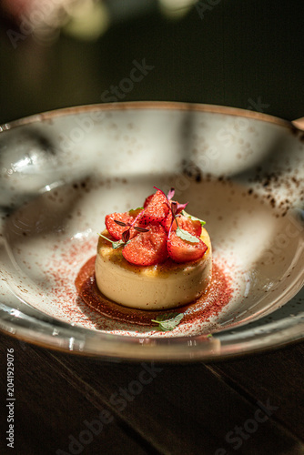 Elegant creme brulee dessert topped with fresh strawberries and caramel sauce on stylish restaurant plate