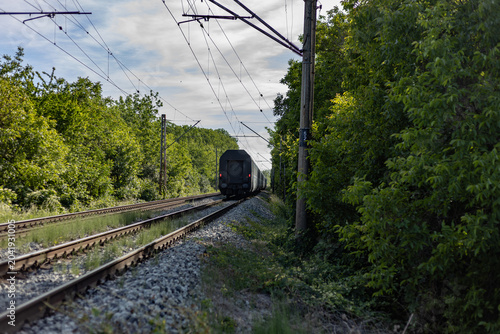 Passenger train moving away through a green summer forest railway