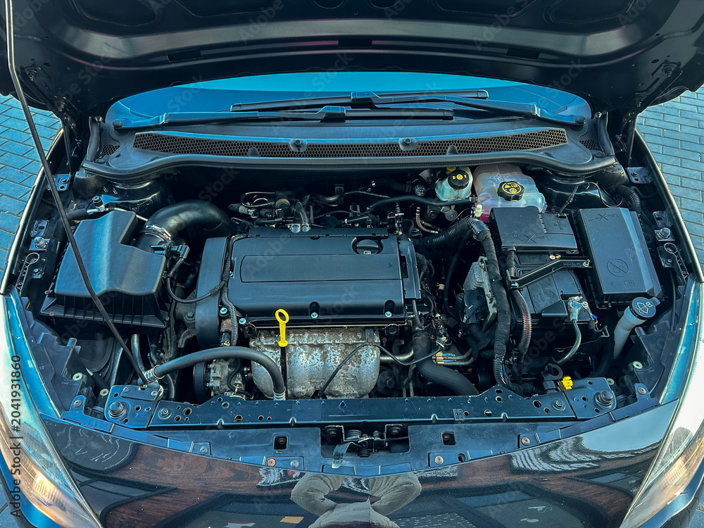 Fototapeta premium Car engine bay shows various parts and components in detail during daylight at a garage or parking area