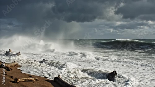 Dramatic ocean waves crashing on a sandy beach under a stormy sky with driftwood scattered along the shoreline