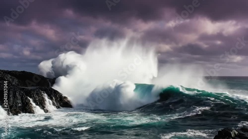 Epic ocean waves crashing against jagged black cliffs under a moody purple and grey cloudy sky
