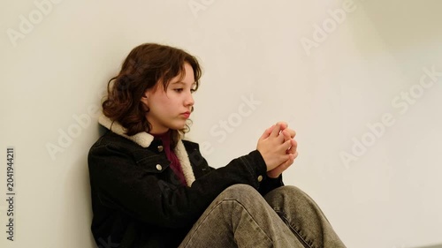 Teen girl in casual denim jacket leans on wall with distant gaze, thinking about problems at school and social media, concept stress anxiety and mental health of modern teenagers.