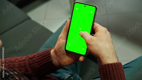 Man holding smartphone with green screen and tracking markers close up over shoulder view. Mobile phone mockup display chroma key space for application web template. Digital device usage