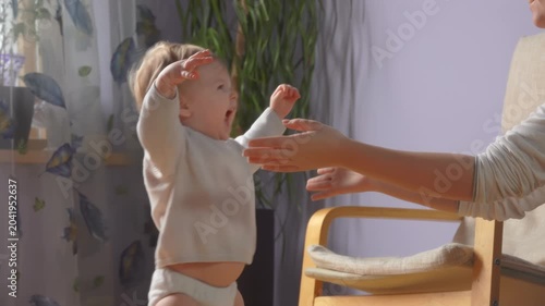 A baby takes first steps walking towards mother who has her arms wide open. Tender family moment of and joy