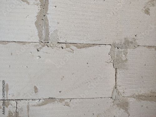 Unfinished lightweight concrete block wall texture with gray cement mortar joints and messy patches.