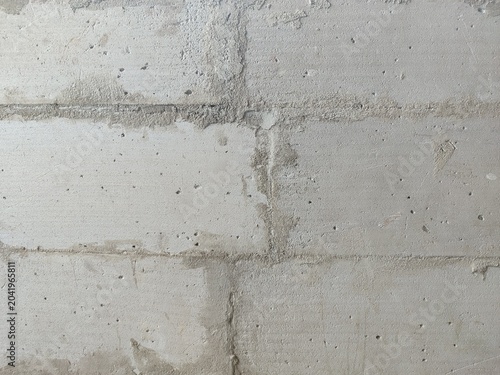 Unfinished lightweight concrete block wall texture with gray cement mortar joints and messy patches.