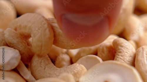 Fingers picking up a single whole cashew nut from a pile. Healthy diet concept. Organic snacking product