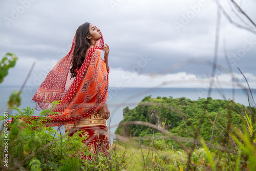 Foto Indonesian Woman Wearing Tenun Ikat on Tropical Coastal Cliff
