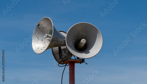 Weathered public address speakers stand tall against bright daytime sky