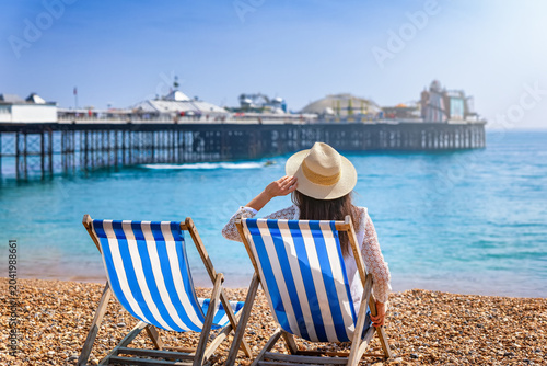 Fotografija A tourist woman sits in a deckchair at the beach of Brighton, England, and looks