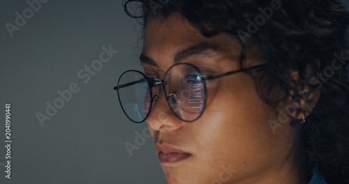 Close-up Black female programmer with code reflection in glasses working late in home office at night. Cybersecurity, AI algorithm, Network security, software developer, serious face, burnout concept.