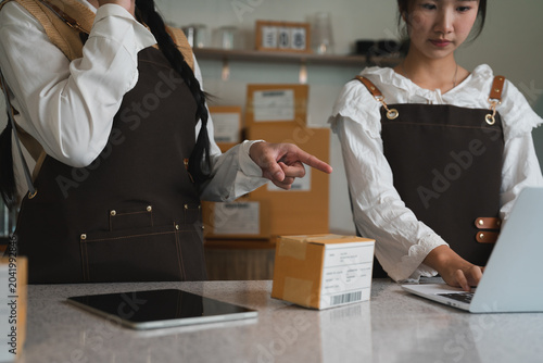 Small business team collaborating on laptop and checking parcel boxes during ecommerce shipping fulfillment and inventory management operations