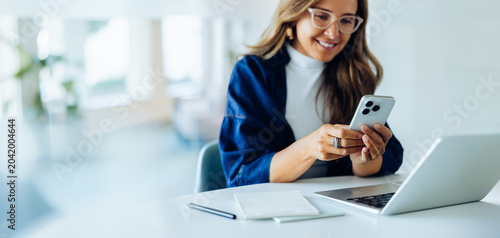 Woman using phone at desk with laptop