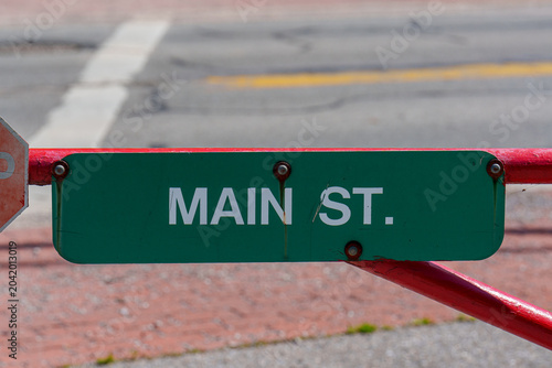 Main St sign visible on a barrier across a street with blurred background showing city features