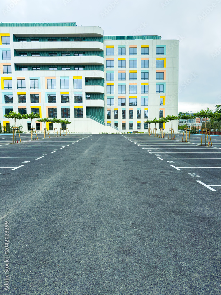 Fototapeta premium Empty parking lot in front of a modern building during a cloudy day with few trees lined along the sides