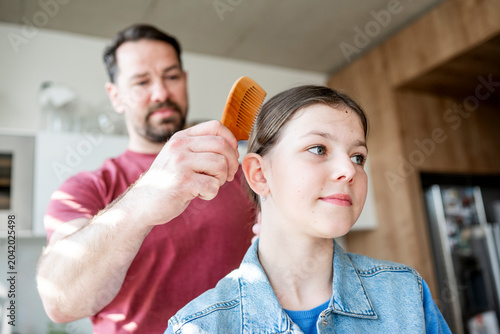 Photos Dad brushing daughter hair and making braid at home.