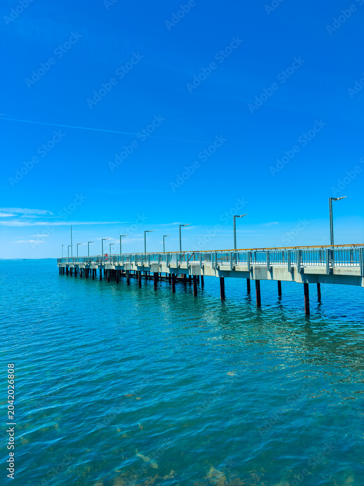 Obraz premium View of a long pier extending into clear blue water on a sunny day with bright sky and few clouds