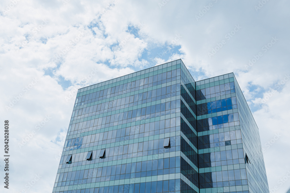 Naklejka premium Tall office building with glass windows under cloudy sky in a city during daytime near the end of summer