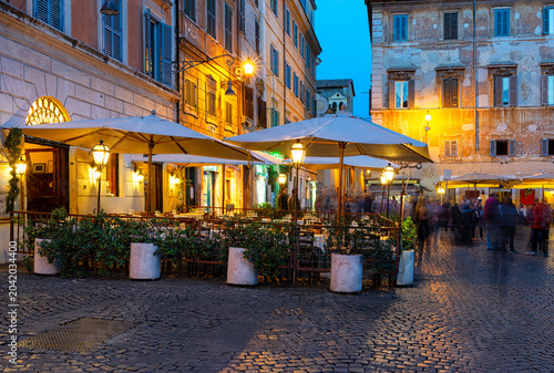 Night cozy old street with tables of restaurant in Trastevere in Rome, Italy. Trastevere is rione of Rome, on west bank of Tiber in Rome. Architecture and landmark of Rome
