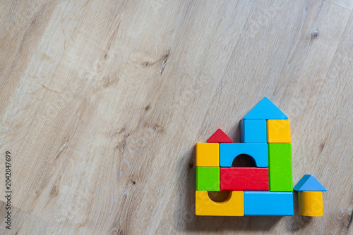 top view of small house built from colorful wooden toy blocks on a light wooden background, with large copy space, for real estate, finance or construction concepts