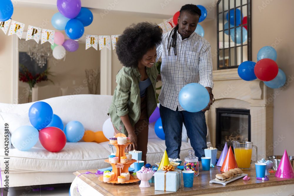Obraz premium Couple standing at coffee table arranging balloons and cupcakes with green overshirt, checked shirt
