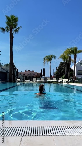 back view of woman swimming in luxury resort pool, authentic summer vacation lifestyle