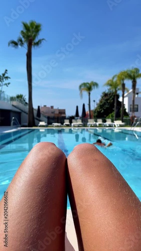 point of view of woman legs sunbathing by a luxury resort swimming pool, authentic summer vacation lifestyle