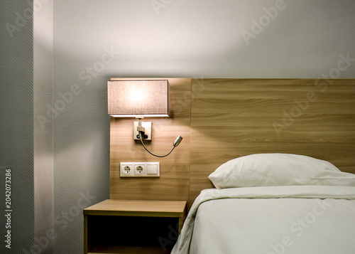 Принти на полотні Modern hotel room interior with wooden headboard, wall mounted lamp, white bedding, bedside table, electrical outlets, minimalist design, contemporary accommodation