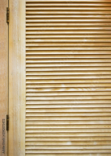 Close-up of wooden louvered door with horizontal slats and visible metal hinges, natural wood texture, ventilation design, architectural detail, ribbed surface background