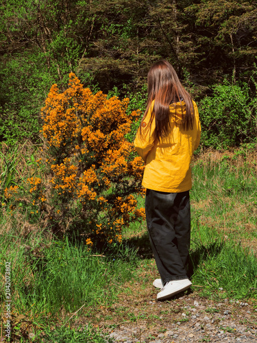 Vászonkép Woman in yellow jacket stands before blooming bush with orange flowers