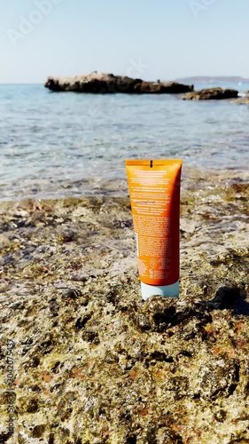 Sunscreen Bottle on Rocks by Clear Blue Sea at Beach.