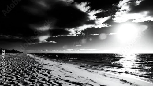 Black and white scenic landscape of beach and ocean during sunset with bright sunlight and dark clouds