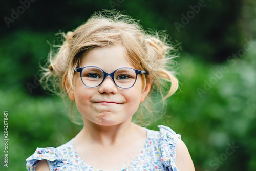 Portrait of funny little girl with glasses making playful face outdoors with messy hairstyle and cheerful expression