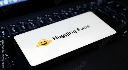 Hugging face logo on smartphone screen resting on computer laptop keyboard