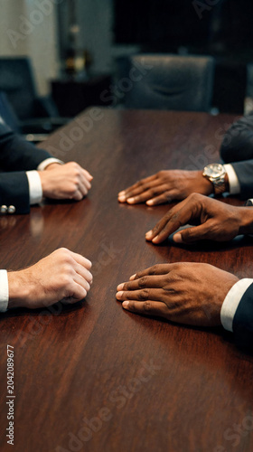 Primer plano de manos de ejecutivos sobre una mesa de madera durante una tensa reunión de negocios. Concepto de negociación, conflicto corporativo y toma de decisiones.
