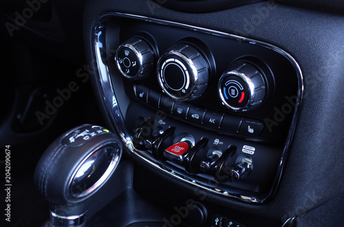 Close up car climate control panel. Premium dashboard climate panel with chrome rings rotary dials for fan temperature and air flow plus illuminated red start engine stop button. It highlights advance
